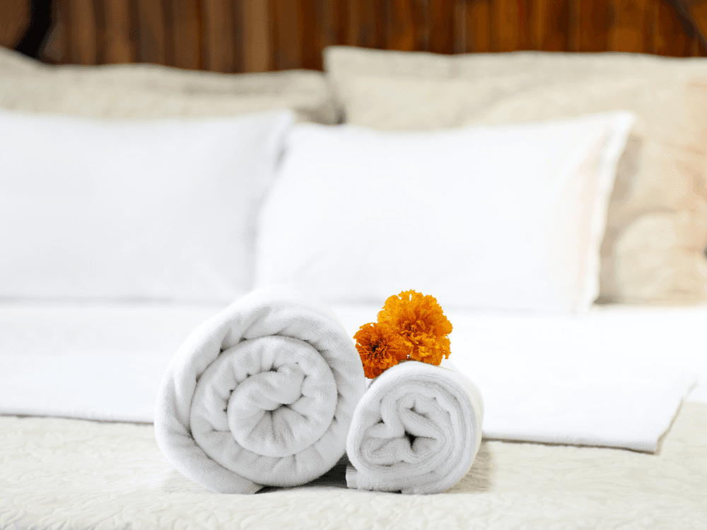 Rolled white towels with marigold flowers on a bed.
