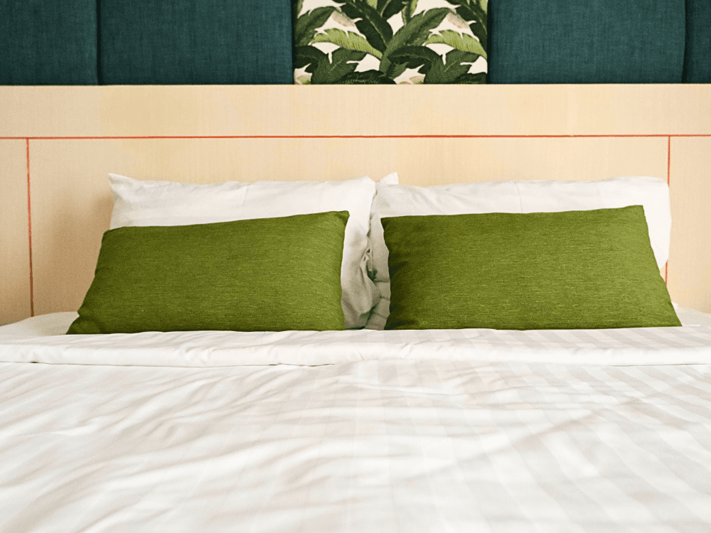 A neatly made bed with two green pillows against a patterned headboard.